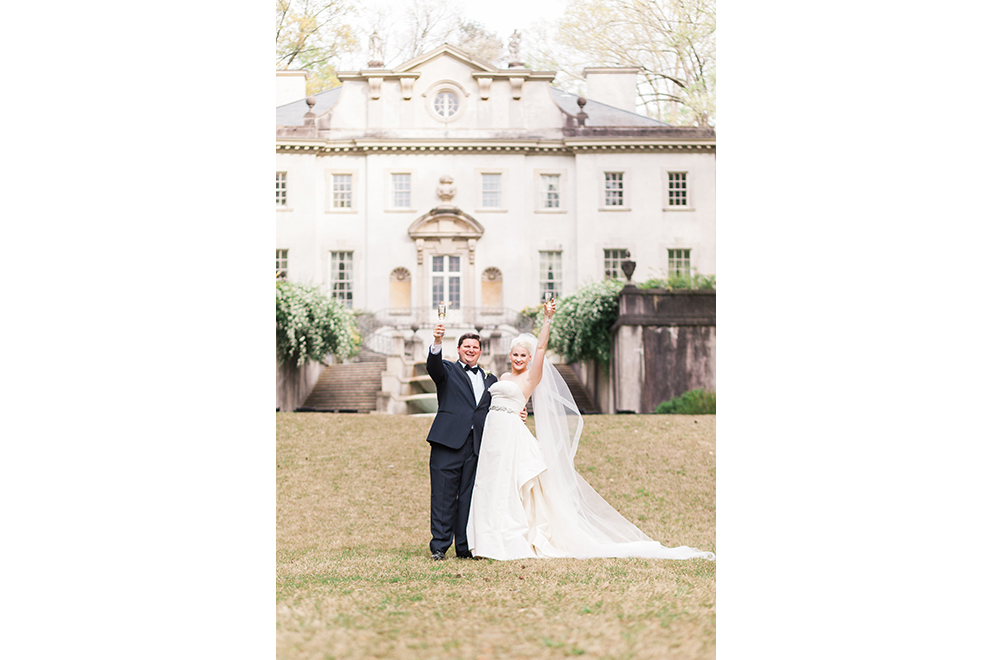 bride and groom in front of The Swan House with glass of champagne